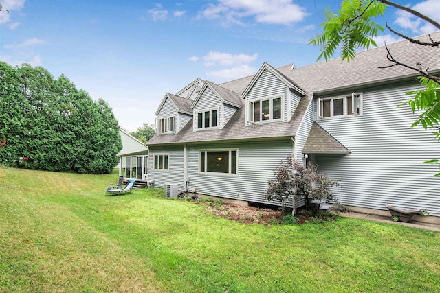 rear view of property featuring central AC unit, a sunroom, a yard, and roof with shingles