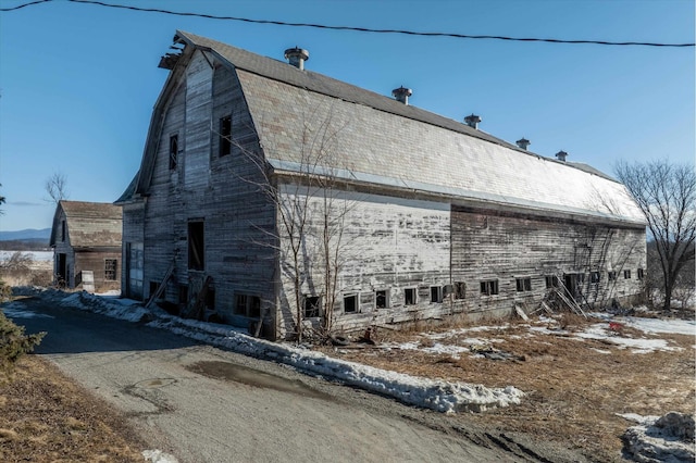 view of snowy exterior featuring a barn, a gambrel roof, and an outdoor structure