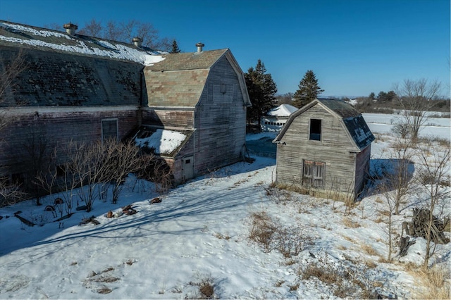 view of snow covered exterior featuring a barn, an outbuilding, and a gambrel roof