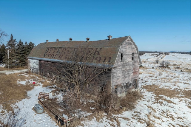 view of snow covered exterior featuring a barn and a gambrel roof