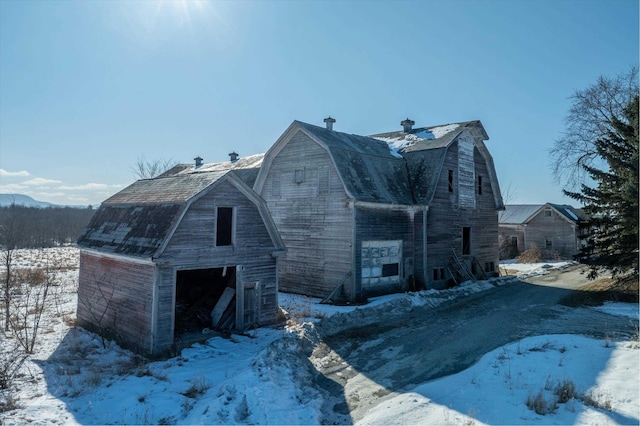 snow covered property with an outbuilding, a garage, a gambrel roof, and a barn