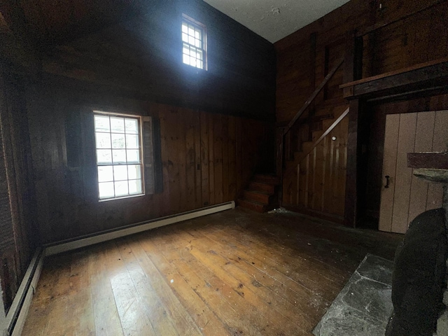 spare room featuring baseboard heating, wood walls, stairs, and wood-type flooring