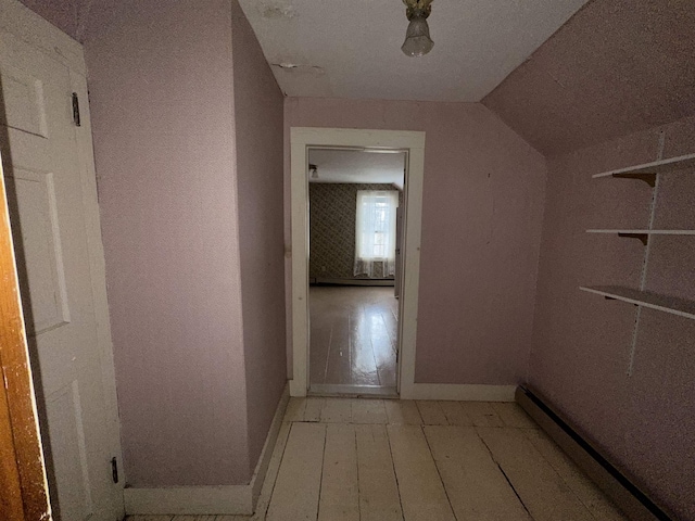 hallway with a baseboard radiator, lofted ceiling, light wood-style floors, and baseboards