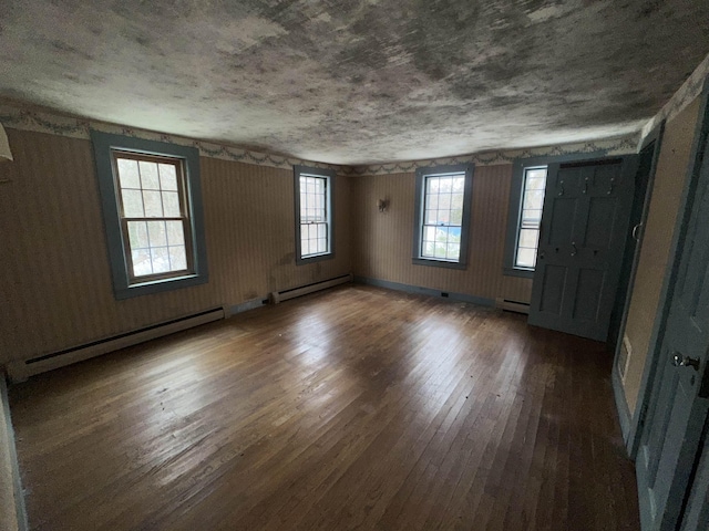 empty room featuring baseboard heating, hardwood / wood-style floors, baseboards, and a baseboard radiator