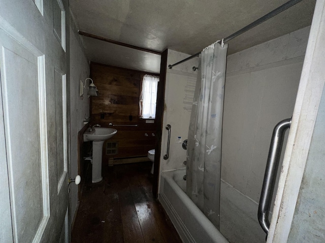 bathroom featuring toilet, hardwood / wood-style flooring, a sink, wood walls, and shower / bath combination with curtain