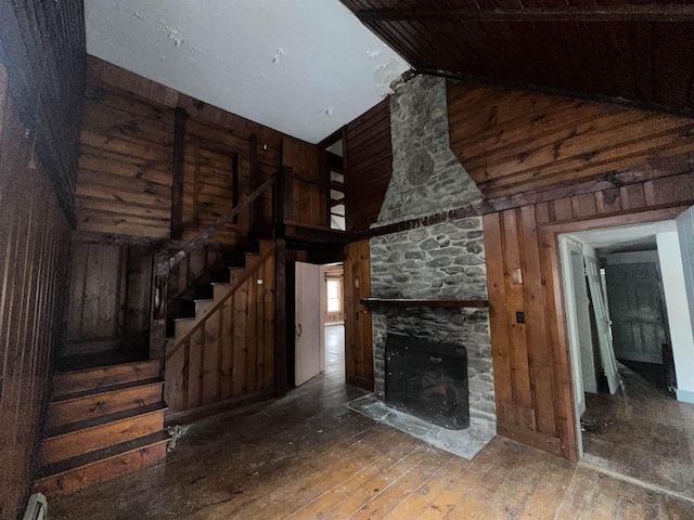 unfurnished living room featuring wood-type flooring, a high ceiling, wood walls, a fireplace, and stairs