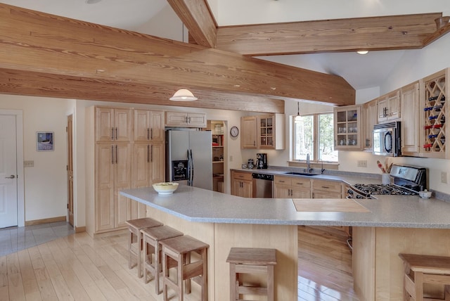 kitchen featuring light brown cabinetry, a sink, stainless steel appliances, a breakfast bar area, and glass insert cabinets