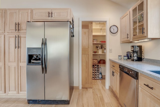 kitchen with glass insert cabinets, light brown cabinetry, light countertops, light wood-type flooring, and appliances with stainless steel finishes