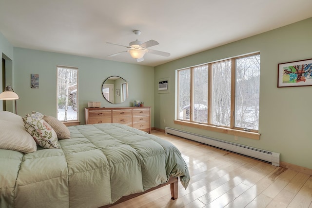 bedroom with a baseboard heating unit, baseboards, a wall mounted air conditioner, light wood-style flooring, and a ceiling fan