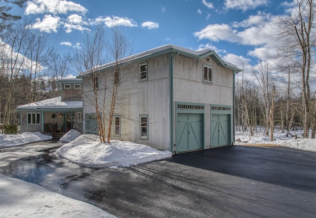 view of snowy exterior featuring an attached garage and driveway