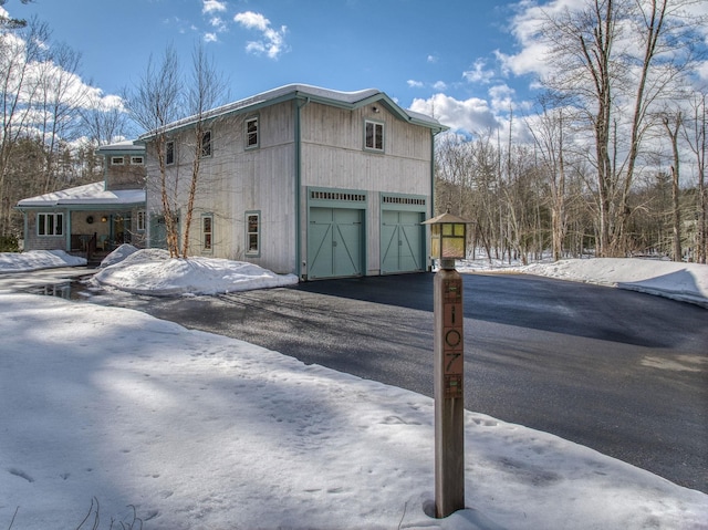 view of snowy exterior featuring driveway and a garage