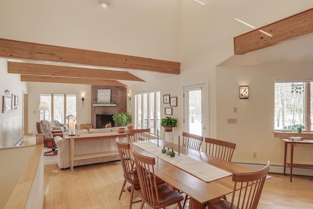 dining room featuring beam ceiling, light wood-style flooring, a brick fireplace, and a baseboard heating unit