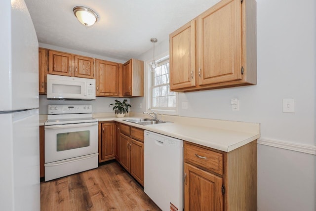 kitchen featuring light wood finished floors, a sink, white appliances, light countertops, and hanging light fixtures