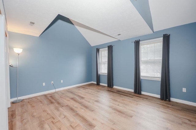 spare room featuring visible vents, baseboards, light wood-style floors, and vaulted ceiling