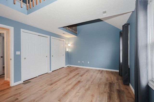 unfurnished bedroom featuring visible vents, baseboards, multiple closets, and wood finished floors