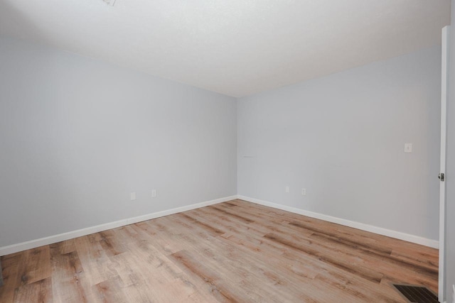 empty room with wood finished floors, visible vents, and baseboards