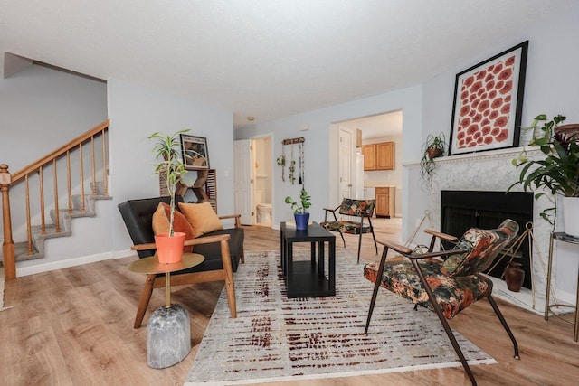 living area featuring light wood-type flooring, stairs, baseboards, and a premium fireplace