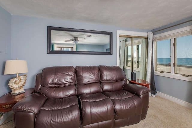 living area with baseboards, plenty of natural light, carpet, and a ceiling fan