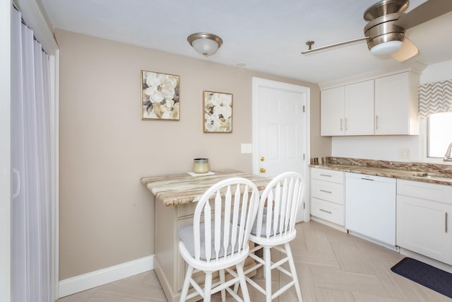 kitchen with baseboards, built in study area, white dishwasher, a sink, and white cabinets