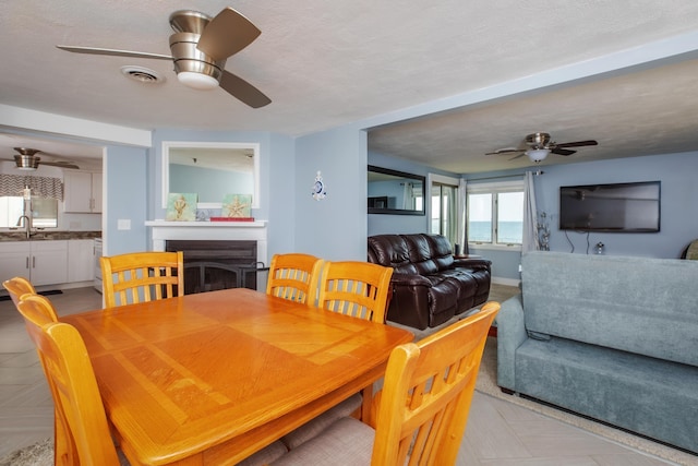 dining room featuring visible vents, a fireplace, a textured ceiling, and ceiling fan