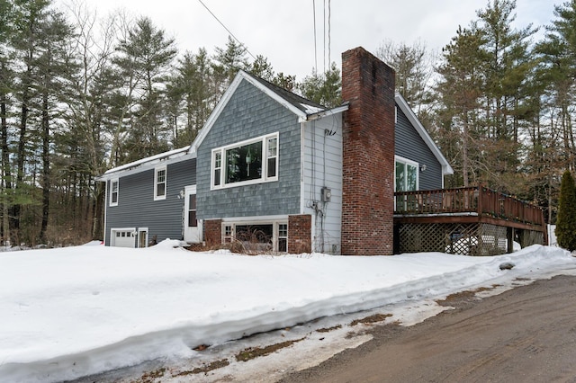 view of snowy exterior featuring a wooden deck, a garage, and a chimney