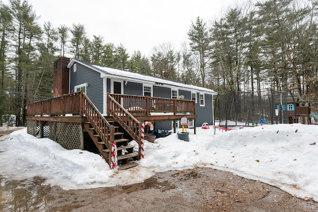 snow covered rear of property with stairs, a trampoline, a deck, and a chimney