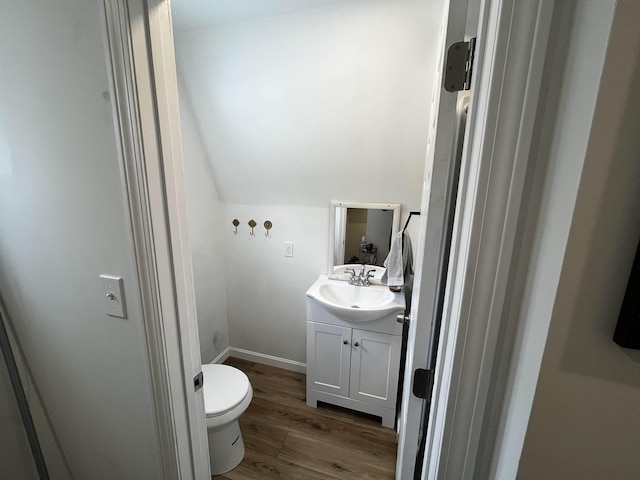 bathroom with baseboards, toilet, vaulted ceiling, wood finished floors, and vanity