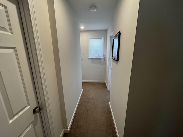 corridor featuring baseboards and dark colored carpet