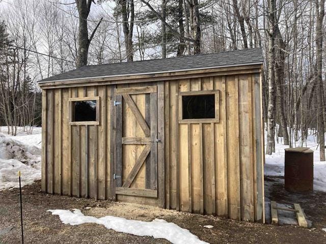 snow covered structure featuring an outbuilding and a storage shed