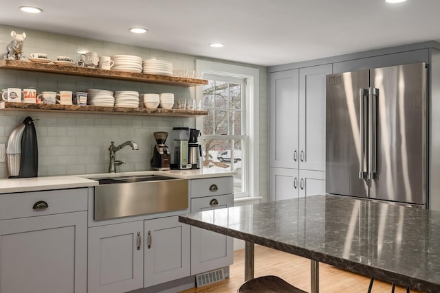 bar featuring visible vents, light wood-type flooring, a sink, backsplash, and high quality fridge