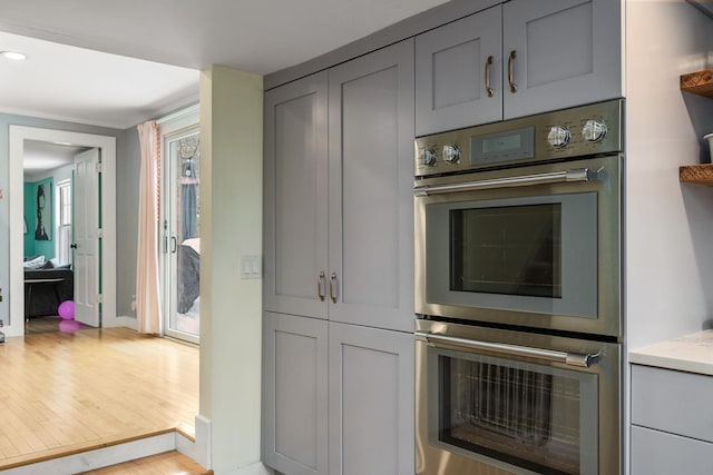 kitchen with light wood finished floors, gray cabinetry, light stone counters, recessed lighting, and stainless steel double oven