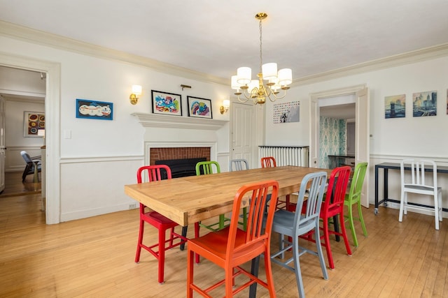 dining room featuring wainscoting, a brick fireplace, light wood-type flooring, and ornamental molding