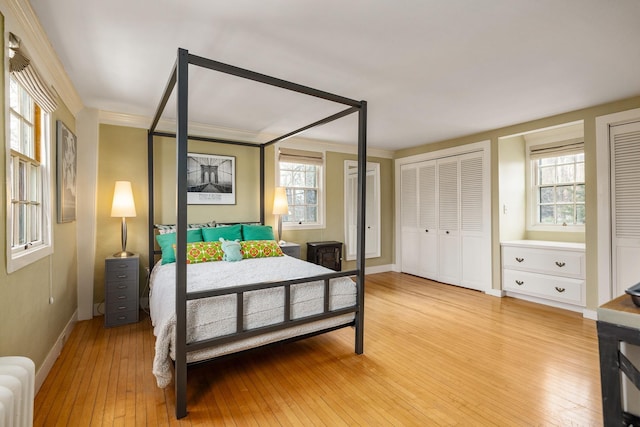 bedroom featuring radiator, crown molding, light wood-style floors, and multiple closets