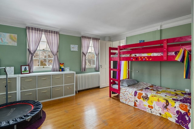 bedroom featuring wood-type flooring, radiator heating unit, and crown molding