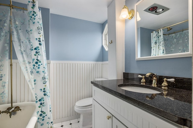 bathroom featuring vanity, a shower with shower curtain, toilet, and wainscoting