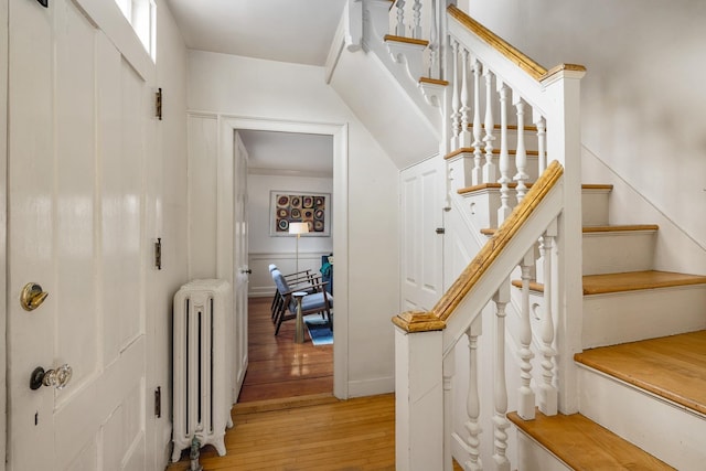 staircase featuring a decorative wall, radiator heating unit, and wood-type flooring