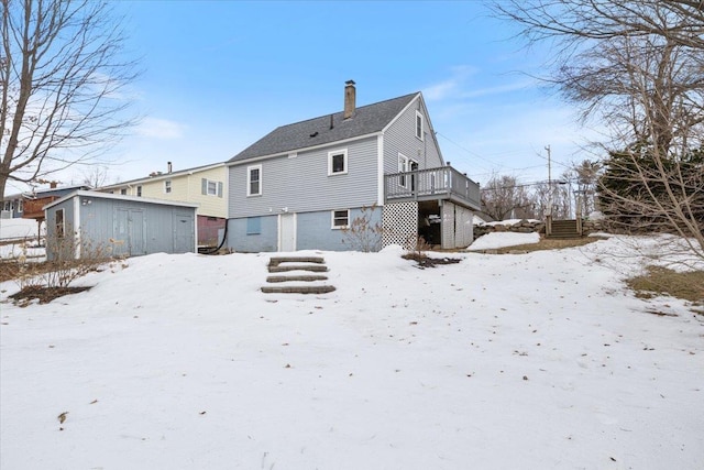 snow covered rear of property featuring stairs, a wooden deck, and a chimney