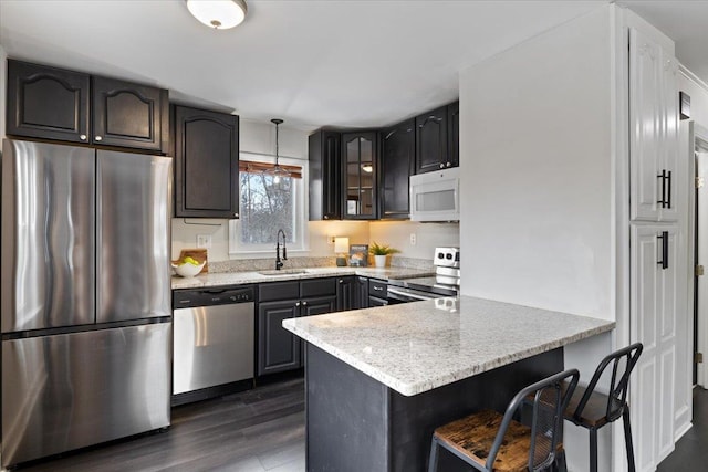 kitchen featuring a sink, a kitchen breakfast bar, dark wood-style floors, appliances with stainless steel finishes, and a peninsula