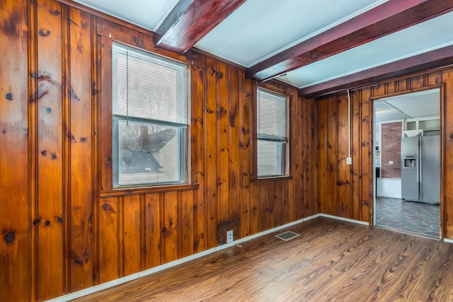 empty room with visible vents, baseboards, wood walls, beam ceiling, and wood finished floors