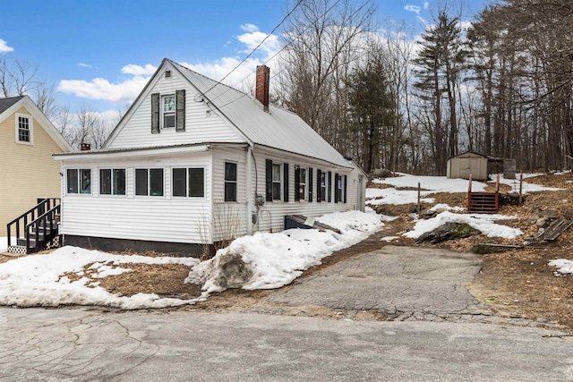 view of front of property featuring a storage unit, an outbuilding, entry steps, metal roof, and a chimney