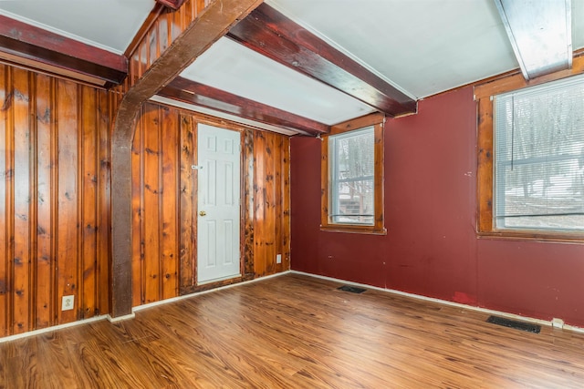 spare room with beamed ceiling, wooden walls, visible vents, and wood finished floors