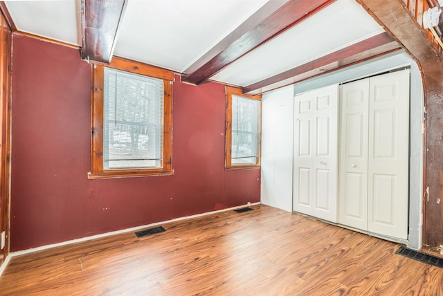 unfurnished bedroom with beamed ceiling, wood finished floors, visible vents, and a closet