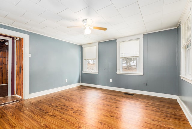 unfurnished room featuring a ceiling fan, wood finished floors, visible vents, and baseboards