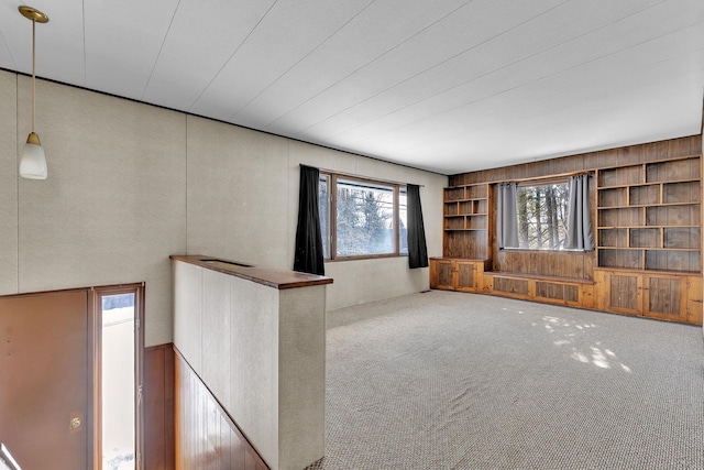 unfurnished living room featuring wooden walls, built in shelves, and carpet floors