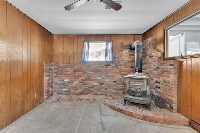 unfurnished living room featuring wooden walls, concrete floors, a wood stove, and ceiling fan