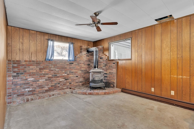 unfurnished living room featuring wooden walls, brick wall, a baseboard radiator, ceiling fan, and a wood stove