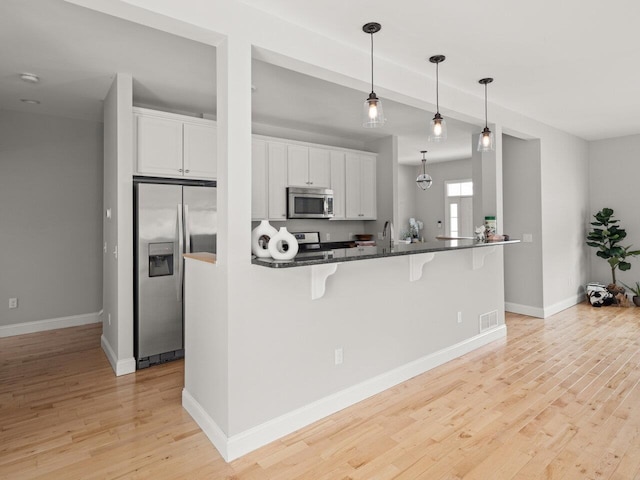 kitchen featuring light wood finished floors, baseboards, a breakfast bar, appliances with stainless steel finishes, and white cabinets