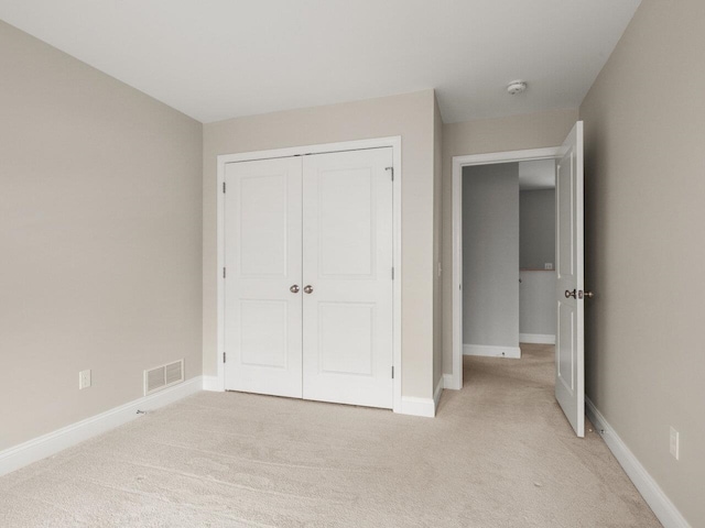 unfurnished bedroom featuring light carpet, visible vents, a closet, and baseboards