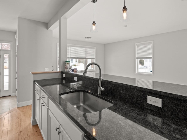 kitchen featuring light wood-style flooring, a sink, decorative light fixtures, white cabinetry, and dark stone counters