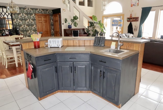 kitchen with a center island with sink, a sink, open floor plan, light tile patterned flooring, and wallpapered walls